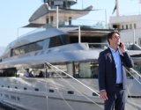 Yacht broker in a suit standing on marina talking on the phone in front of a luxury yacht