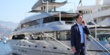 Yacht broker in a suit standing on marina talking on the phone in front of a luxury yacht